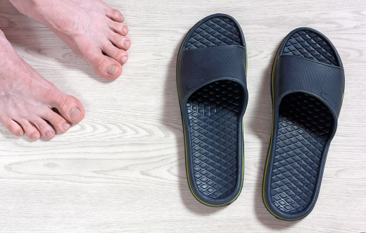 Male bare feet next to a pair of blue flip-flops on a white wooden floor