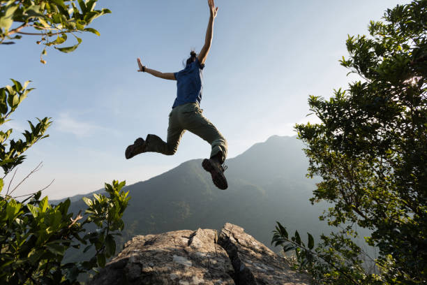 istock young woman jumping on cliff's edge with raised hands to the sunrise 873207886