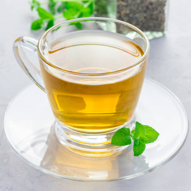 istock Herbal mint tea in glass cup with fresh peppermint on background, square format 873212156