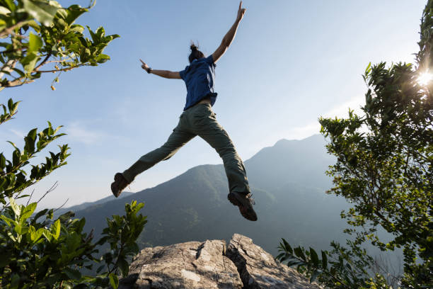 istock young woman jumping on cliff's edge with raised hands to the sunrise 873212314