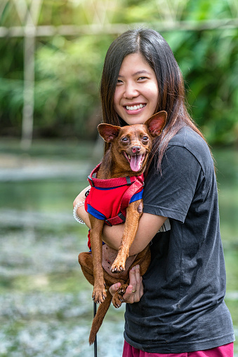 The asian women mini dog in brown color over the lake at the resort in deep forest, Lover and animal with nature concept