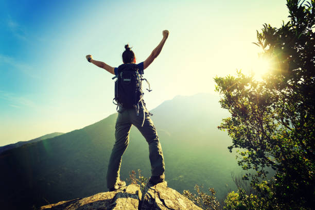 istock young woman backpacker standing on cliff's edge with raised hands 873222750