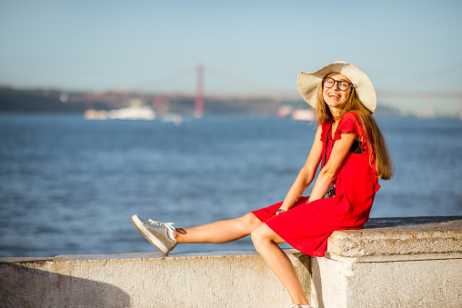 Young woman sitting on the riverside with landscape view on the bridge in Lisbon city, Portugal