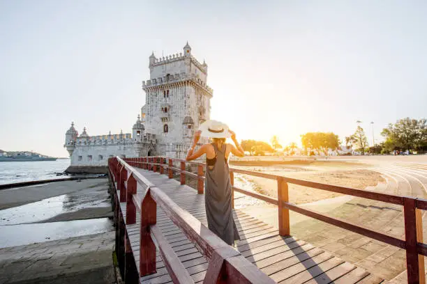 Young woman tourist walking on the bridge of the Belem tower on the riverside during the sunset in Lisbon, Portugal