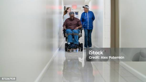 The Disabled Africanamerican Man In Wheelchair Accompanied With Black Woman And White Teenager Girl In The Corridor Of The Residential Living Building In Bronx Stock Photo - Download Image Now