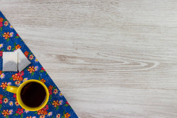 Tea mug on pattern flower cloth napkin on empty wooden background. Top view with space for your text.