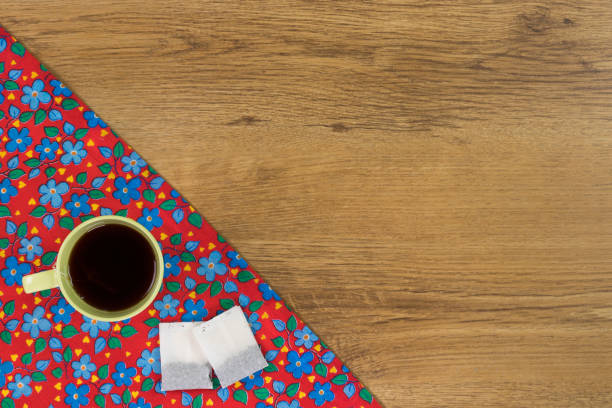 Tea mug on pattern flower cloth napkin on empty wooden background. Top view with space for your text.