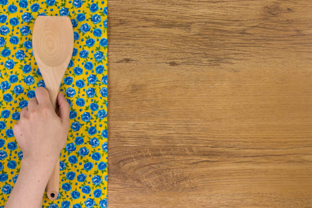 istock Hand holding kitchen wood spoon.  Pattern flower cloth napkin on empty wooden background. 873290000