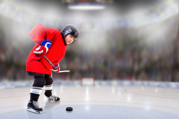 Low angle view of hockey player handling puck on ice with sports arena full of fans in the stands and copy space. Shallow depth of field on background. Fictitious arena background created entirely from scratch in Photoshop. Model was shot in studio on Dec. 30, 2016, and then composited onto fictitious arena.