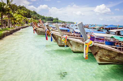 Thai wooden boats in the clear water of the ocean with blue cloudy sky on the background