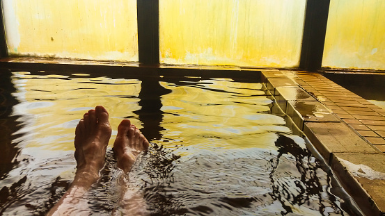 Female enjoying hot spring water against steamed window, personal perspective, just feet in water, Hokkaido, Japan