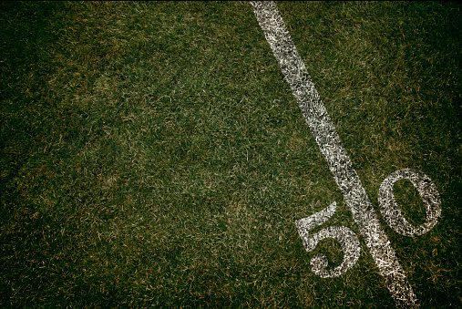 Football field ground fifty yard line. Friday night lights.