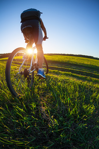 Young man cycling on a rural road through green spring meadow during sunset
