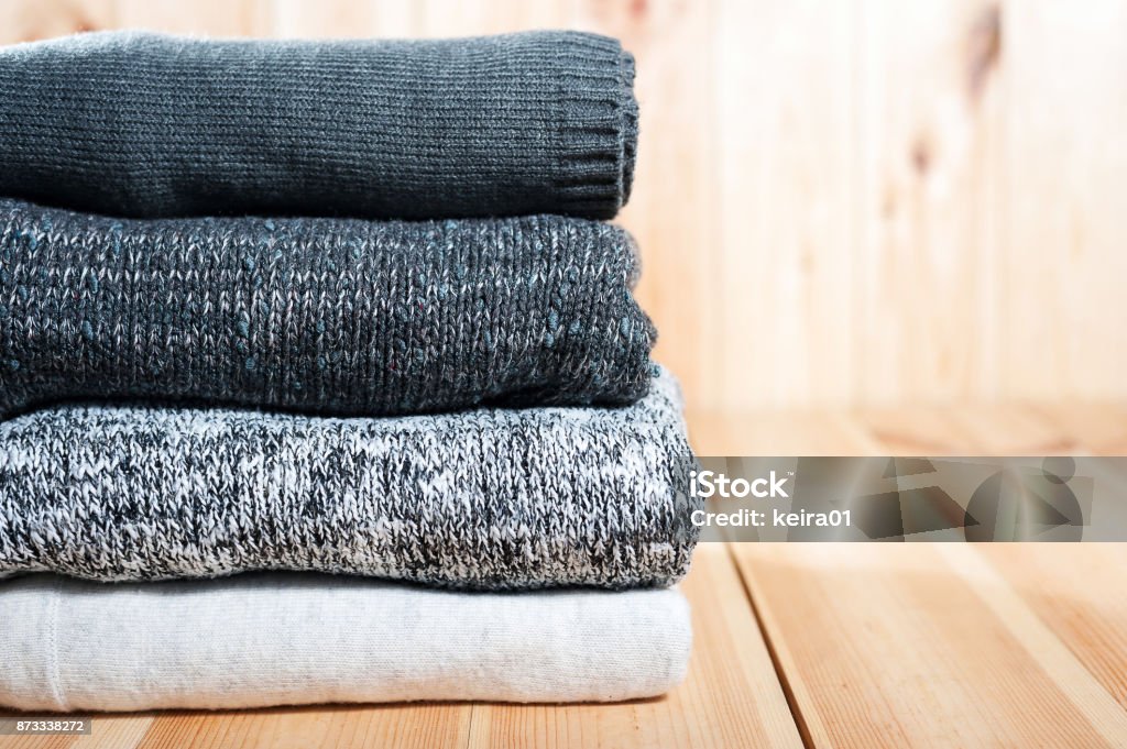 A neat pile of knitted warm blanket or sweaters gray, white on a wooden background. A neat pile of knitted warm blanket or sweaters gray, white on a wooden background. Comfort, warmth and a homely atmosphere in the cold winter. Copyspace Blanket Stock Photo