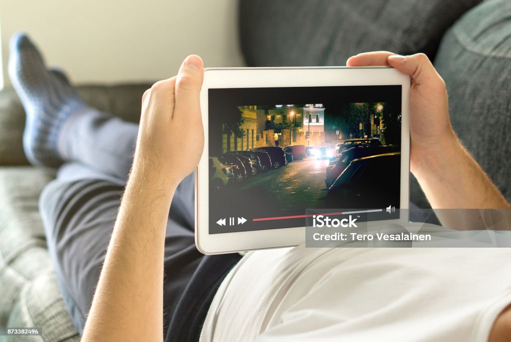 Online movie stream with mobile device. Online movie stream with mobile device. Man watching film on tablet with imaginary video player service. Downloading Stock Photo