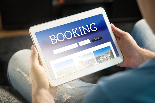 Booking app or website on tablet screen. Man searching hotel and flights for holiday and vacation with travel application. Person holding smart device in hand.