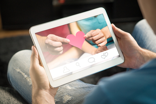 Online dating concept. Imaginary application or website. Finding love from internet using app. Man using and holding tablet and smart device at home.