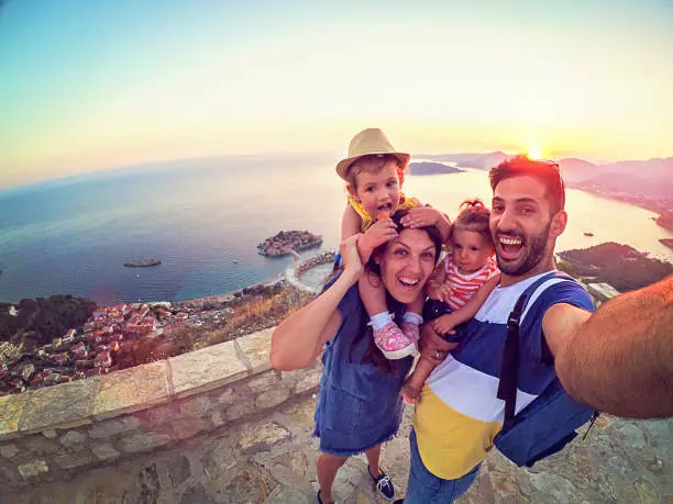 Photo of Family with two little daughters travel in nature, making selfie, smiling