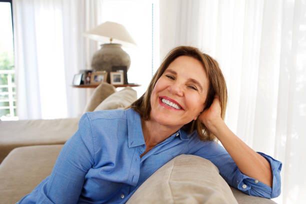 istock older woman smiling at home on sofa 873392838