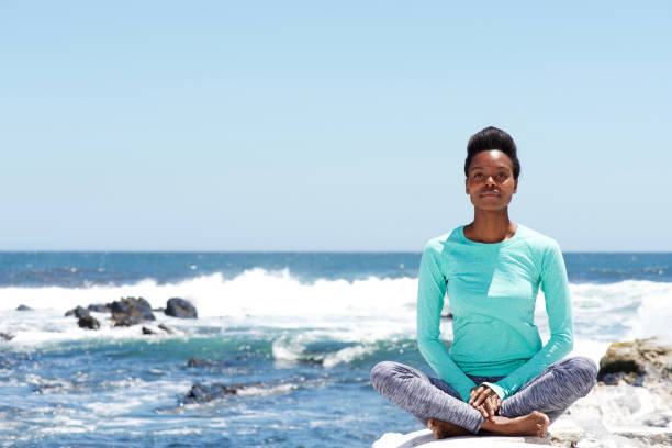 junge afrikanische amerikanische frau, die beim yoga am strand - zen like nature breathing exercise sitting stock-fotos und bilder