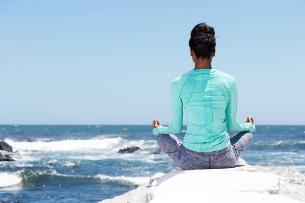 hinter der yoga-frau am strand - zen like nature breathing exercise sitting stock-fotos und bilder