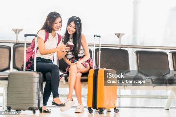Two Young Asian Girl Using Smartphone Check Flight Or Web Checkin Sit At Airport Waiting Seat Together Air Travel Lifestyle Exciting Summer Vacation Trip Or Mobile Phone Gadget Application Concept Stock Photo - Download Image Now