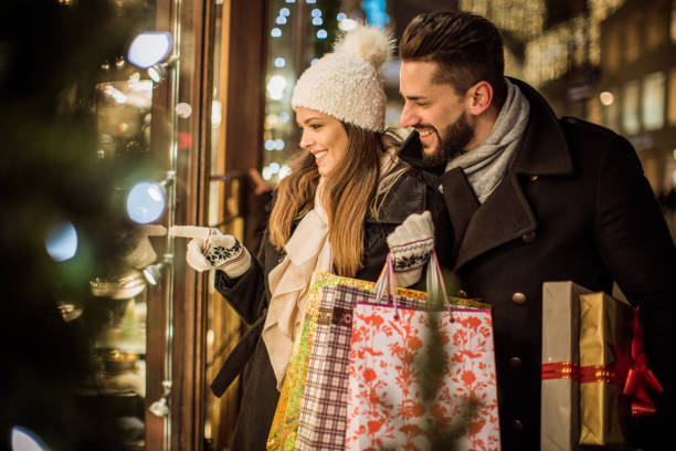 Joy of buying Christmas gifts Young couple walking in downtown for Christmas. Holding Christmas gifts and big Teddy bear. Wearing warm clothing. holiday shopping stock pictures, royalty-free photos & images