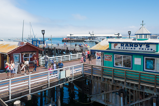Monterey, California, USA-August 1, 2014: Pier in the Harbour of Monterey, California, with some boats, stores, some people, and an office for whale watching. A USA flag on the left lower corner.