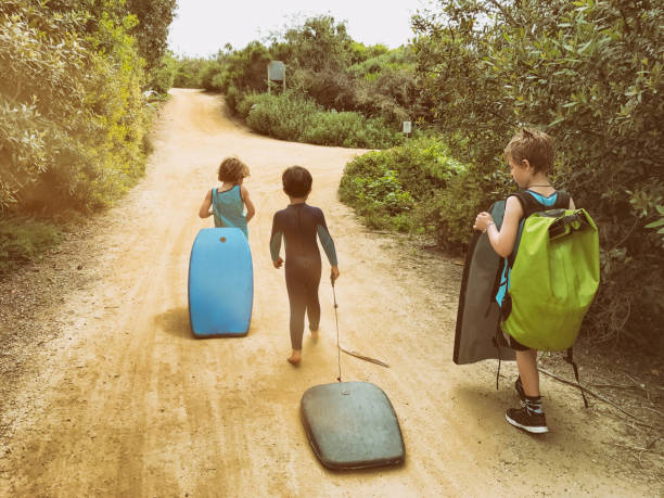 famille de garçons à pied à la plage ensemble tout en transportant leurs planches de boogie - fitness trainer photos et images de collection