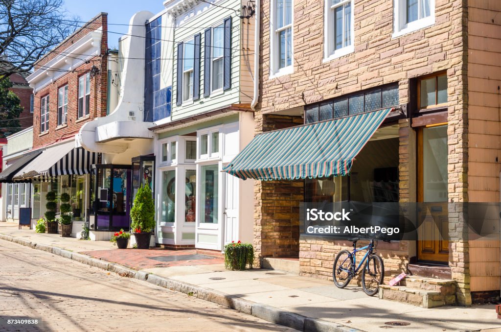 Traditional American Stores along a Cobble Street Traditional American Stores along a Cobblestone Street in the Historic District of Annapolis, MD, on a Sunny Autumn Day. There is a Bicycle Leaning against the Window of one of the Stores. City Street Stock Photo