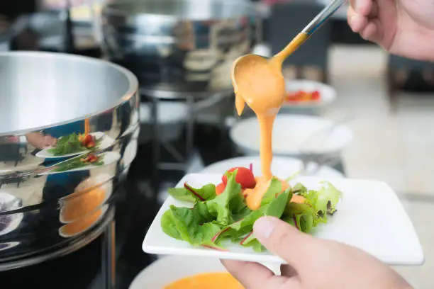 Photo of Tablespoon measure of creamy thousand island dressing being poured over fresh garden salad in breakfast buffet at hotel.