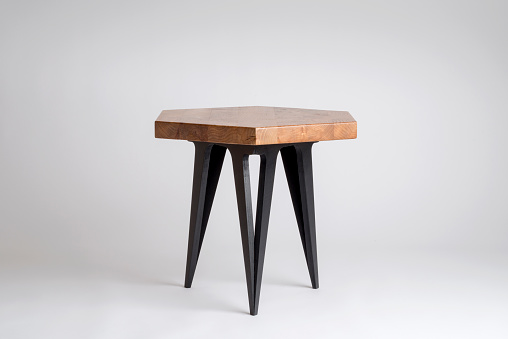 Modern wooden stool or small table with hexagonal top and black painted legs isolated on white background