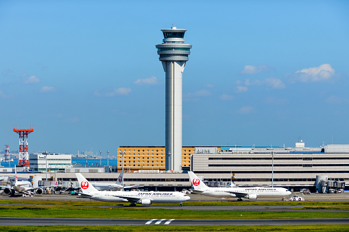 Various aircraft line up to taxi to the runway at Tokyo Haneda Airport. Photo taken during a warm fall afternoon. In addition to the airplanes, there are other support and service vehicles moving about.