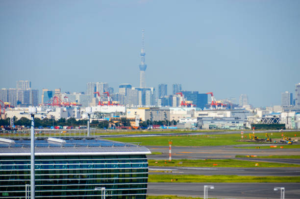 Various aircraft line up to taxi to the runway at Tokyo Haneda Airport. Photo taken during a warm fall afternoon. In addition to the airplanes, there are other support and service vehicles moving about.