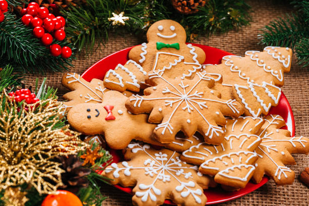 biscuits de noël pain d’épice maison en plaque rouge avec des branches d’arbre de noël et du nouvel an décor sur table avec nappe de toile de jute. carte postale de la noël joyeux. - pain dépice photos et images de collection