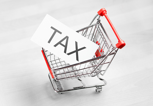 Tax, taxation and VAT concept. Shopping cart with a card or paper sign.