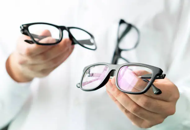 Photo of Optician comparing lenses or showing customer different options in spectacles. Eye doctor showing new glasses.