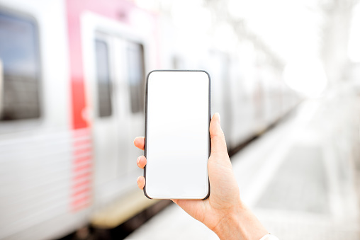 Holding a smarphone with empty screen with train on the background at the railway station