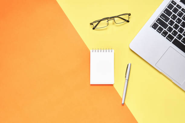istock Top view, Modern workplace with laptop and notebook with pen placed on a pastel yellow background. Copy space suitable for use in graphics. 873473542