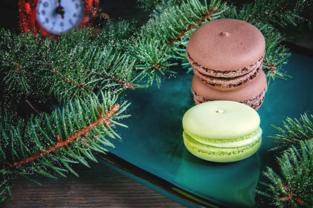 istock Fresh green and brown macaroons on Christmas table decorated with fir branches with a clock on . Copy the place 873480312