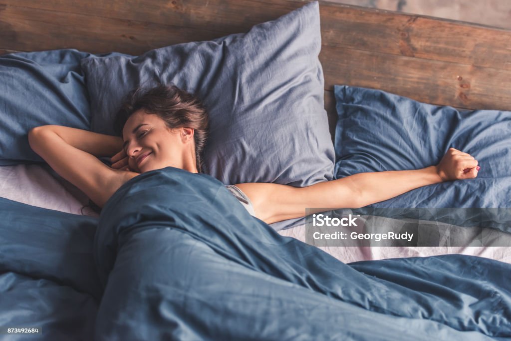 Young woman in bed Beautiful young woman is stretching and smiling while lying in bed in the morning Sleeping Stock Photo