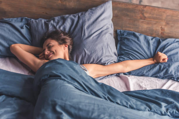 Young woman in bed Beautiful young woman is stretching and smiling while lying in bed in the morning duvet stock pictures, royalty-free photos & images