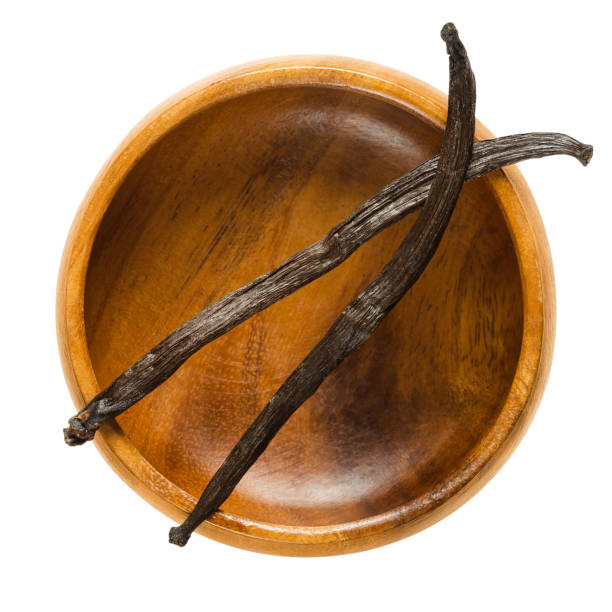 Dried Bourbon vanilla pods over empty wooden bowl Dried Bourbon vanilla pods over empty wooden bowl. Two dark brown ripe fruits of Vanilla planifolia. Spice with distinctive flavor, used in baking. Macro food photo close up from above over white. vanilla orchid stock pictures, royalty-free photos & images