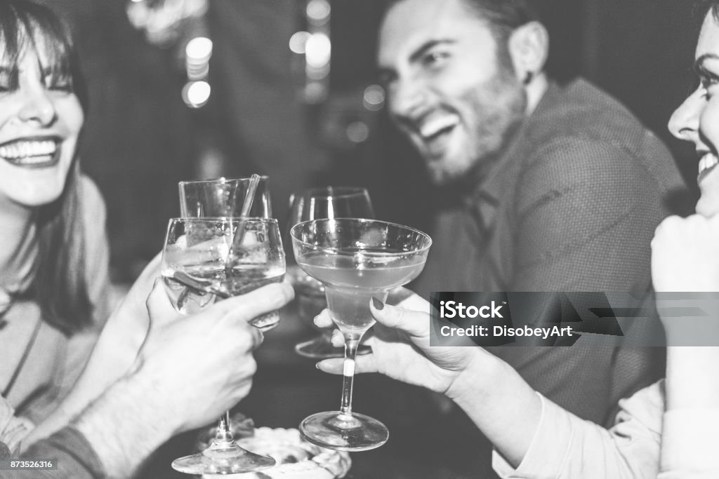 Happy friends cheering at cocktail jazz bar - Young trendy people having fun drinking alcohol and laughing - Party concept - Focus on right woman hand glass - Black and white editing - Warm filter Restaurant Stock Photo