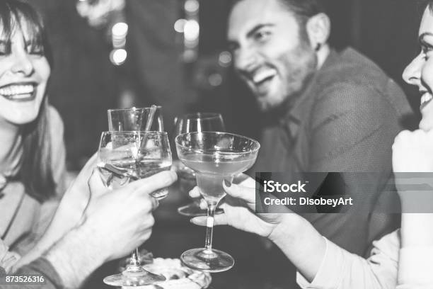 Happy Friends Cheering At Cocktail Jazz Bar Young Trendy People Having Fun Drinking Alcohol And Laughing Party Concept Focus On Right Woman Hand Glass Black And White Editing Warm Filter Stock Photo - Download Image Now