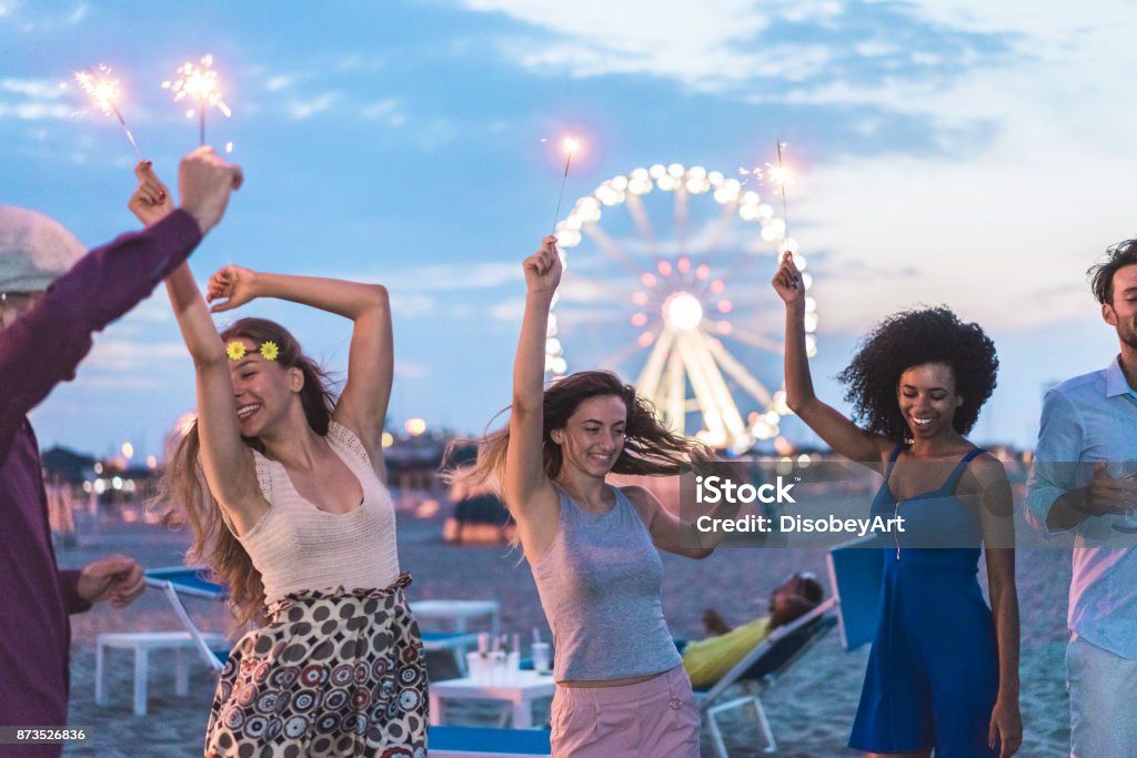 Felizes amigos fazendo a festa na praia depois do anoitecer com fogos de artifício e bebendo champanhe - jovens se divertindo dançando ao ar livre - Soft concentrar no rosto de garota centro - juventude e conceito de festival - Foto de stock de Miami royalty-free