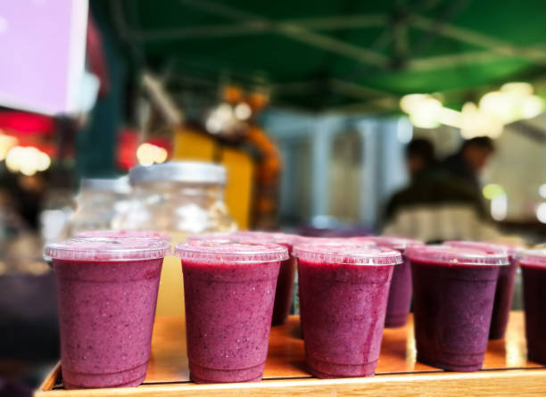 Freshly made fruit smoothies in a row at the food market, Borough Market, UK Close up color image depicting freshly made fruit smoothies in a row on a wooden counter at the food market - specifically Borough Market in London, UK. The smoothies are purple or pink in color and appear to have been made with strawberries, blackberries or blueberries, or a combination of berries. In the background, the people working on the market stall are blurred out of focus, Room for copy space. juice bar stock pictures, royalty-free photos & images