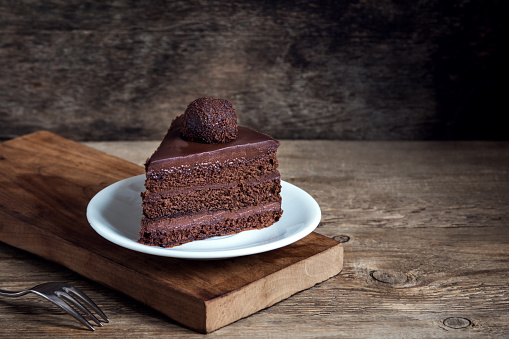 Cut puff chocolate piece from a cake on a white plate.