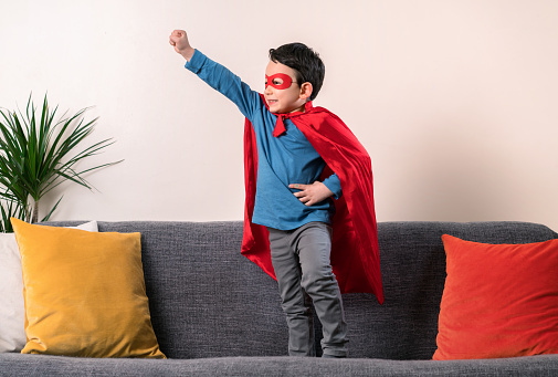 A cute kid is playing and pretending to be a superhero with his hero costume