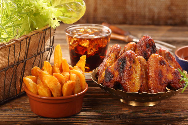 Chicken wings with baked potatoes and cold drink on wooden background\